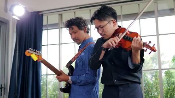 Dos hombres asiáticos tocan instrumentos clásicos violín y guitarra juntos en una sala de práctica musical. A ambos les gusta tocar música. Concepto de tocar música en vivo y bandas - Metraje, vídeo
