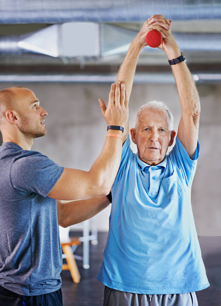 Ascensor para la longevidad. Fotografía de un hombre mayor haciendo ejercicio con la ayuda de un entrenador. - Foto, Imagen