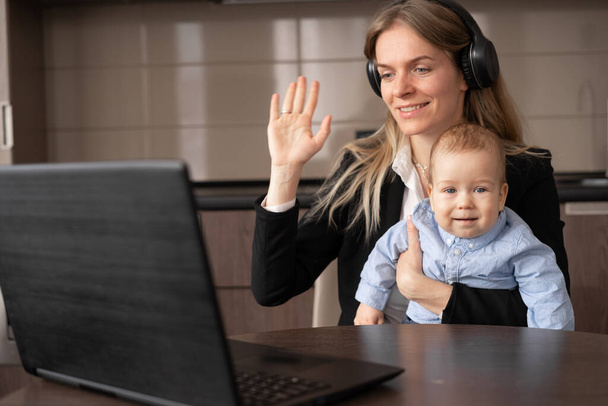 Glückliche junge kaukasische alleinerziehende Mutter, die ihren kleinen Sohn am Laptop hält, Frau, die von zu Hause aus arbeitet, Videotelefonate, virtuelle Fernbesprechung, Beraterin mit Kopfhörer, Lebensstil in Karenz - Foto, Bild