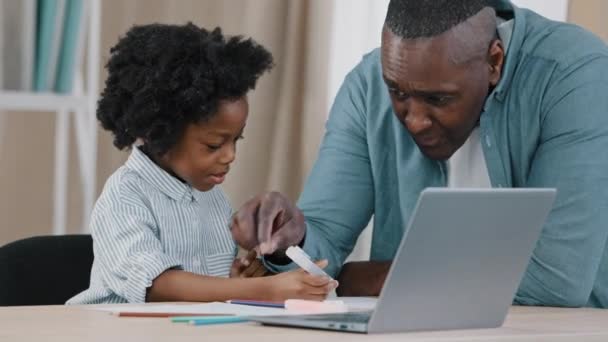 机に座って宿題をする小さなアフリカ系アメリカ人の子供の女の子成熟したお父さんは、家庭教師の家庭教師の家庭教師と娘が隔離中に個々のレッスン距離学習を行うのを助ける - 映像、動画