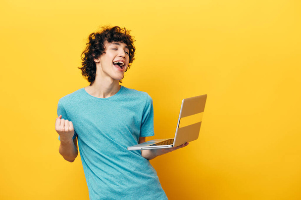 curly guy in blue t-shirts with laptop internet yellow background - Φωτογραφία, εικόνα