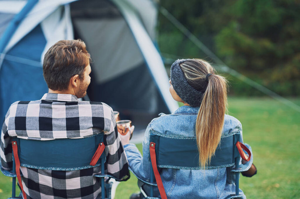 Junges nettes Paar sitzt auf Stühlen vor dem Zelt auf dem Campingplatz - Foto, Bild