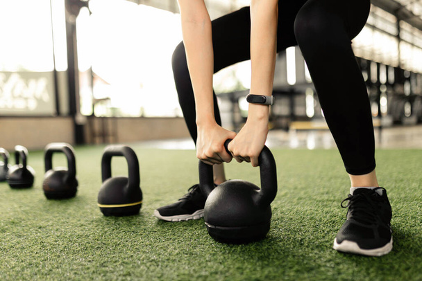 exercise concept The black kettlebells being lined on the green carpet for being done kettlebell swing by someone who wears a grey smartwatch and black pair of shoes. - Photo, Image