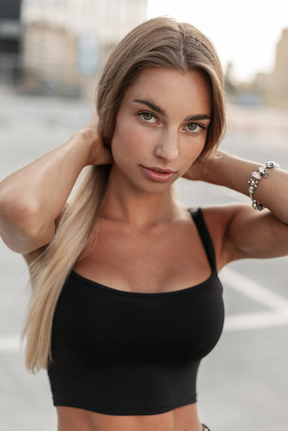 Beautiful young woman in a stylish mockup black T-shirt with a fashion bracelet on her arm looks at the camera in the city - Zdjęcie, obraz
