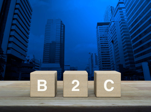 B2C acronym on wood block cubes on wooden table over modern office city tower and skyscraper, Business to customer marketing and strategy concept - Foto, Imagem