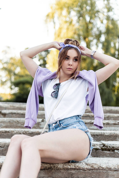 Elegante bella ragazza in abiti alla moda estate casual si siede sui gradini del parco - Foto, immagini