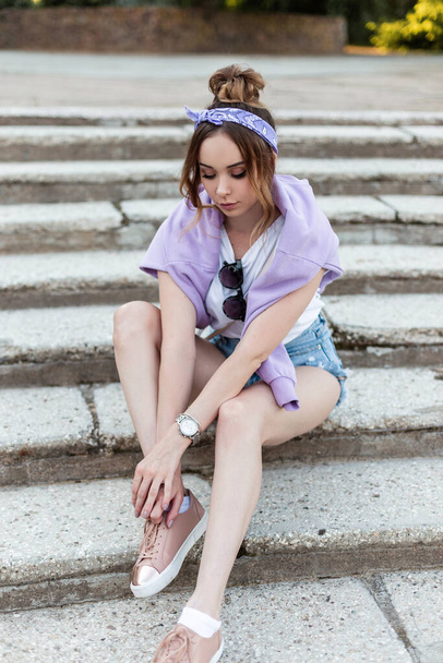 Pretty woman with bandana in fashion casual clothes and accessories with shoes sits on the steps - Photo, Image