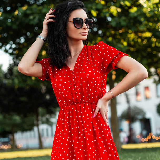 Femme modèle élégant avec des lunettes de soleil à la mode en robe rouge vintage marche à l'extérieur - Photo, image