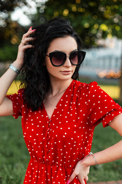Pretty curly woman with fashion sunglasses and watch in red dress walking outdoors - Foto, Imagem