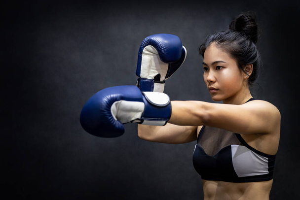 Giovane donna asiatica boxer in posa uppercut con guanti da boxe blu in palestra fitness. Lezione di boxe femminile. Concetto di arti marziali - Foto, immagini