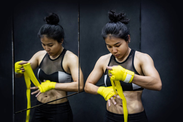 Asian female boxer wearing yellow cotton bandage strap on wrist in fitness gym. Athlete woman with muscular body preparing for boxing sport. Martial arts concept - Photo, Image