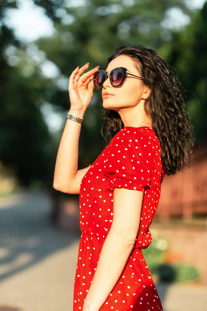 幸せな若いです女性でファッションサングラスでヴィンテージ夏赤ドレス散歩で街で日没 - 写真・画像