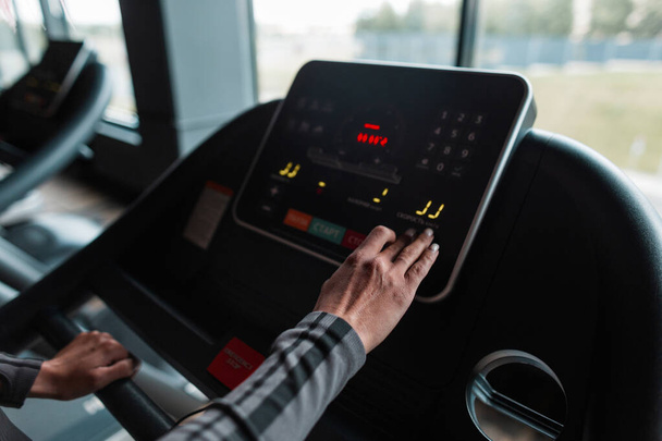 Woman chooses a mode on a treadmill before jogging in a gym, close up - Photo, Image