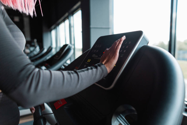Young athletic woman starts jogging on treadmill and chooses running mode - Foto, afbeelding