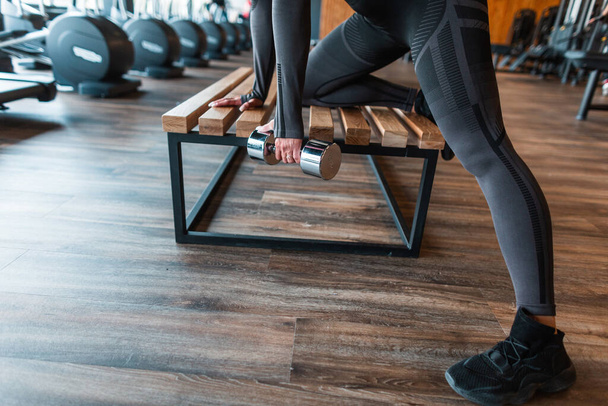 Žena sportovec v černém oblečení s činky cvičení na dřevěné lavičce v tělocvičně - Fotografie, Obrázek