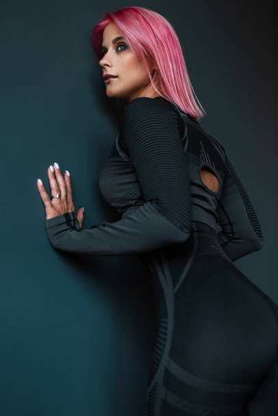 Фитнес-женщина с красивым атлетическим телом позирует у черной стены - Фото, изображение