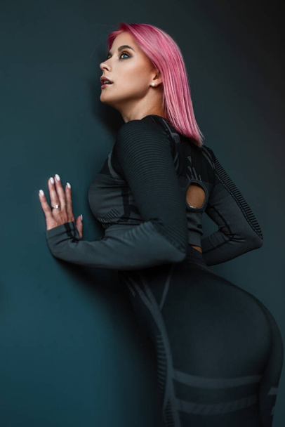 beautiful young model woman fitness trainer in black sportswear posing near black wall - Fotó, kép