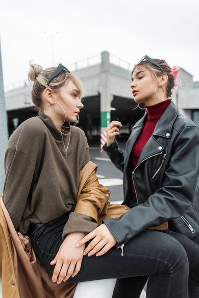 Beautiful young teen girls in fashionable clothes sit on the street in the city - Photo, Image