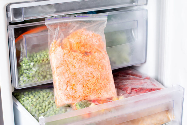Zanahorias ralladas congeladas en una bolsa en el congelador. Alimentos congelados - Foto, imagen