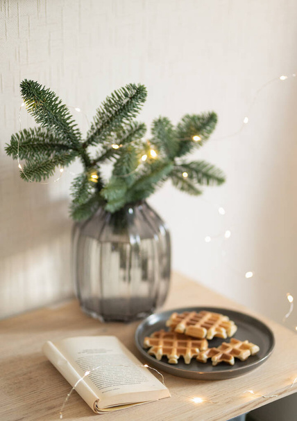 Petit déjeuner du Nouvel An avec gaufres sur une assiette et un livre, branche d'arbre de Noël dans un vase - Photo, image