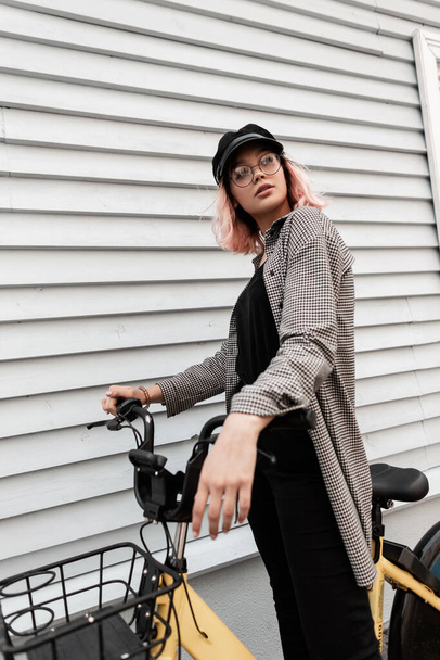 Mujer bastante joven hipster en ropa casual de moda con bicicleta de paseo cerca de la pared de madera en la calle - Foto, Imagen