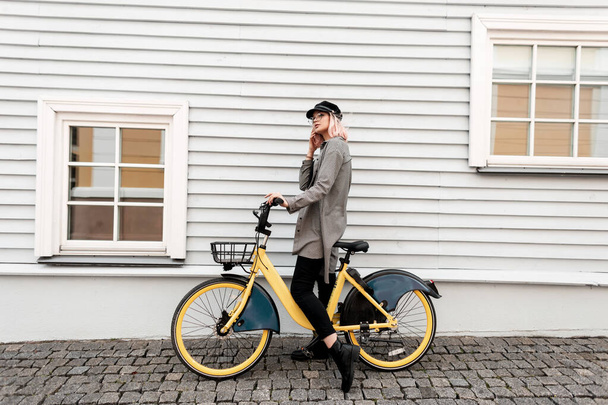 Fiatal, gyönyörű hipszter lány divatos ruhákban és kockás ingben biciklivel egy faház mellett - Fotó, kép
