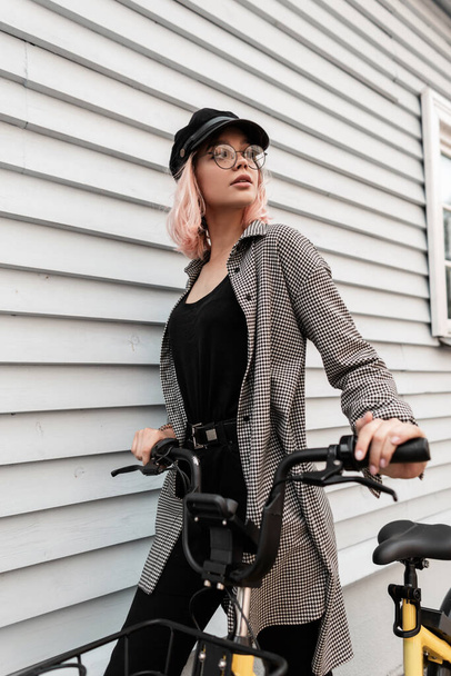 Moda kıyafetleri içinde, eski gözlüklü, güzel hippi kız. Bisikletli, ahşap bir evin yanında duruyor. - Fotoğraf, Görsel