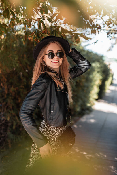 Mulher sorridente muito elegante em look de roupa de moda com jaqueta de couro e vestido vintage anda ao ar livre - Foto, Imagem