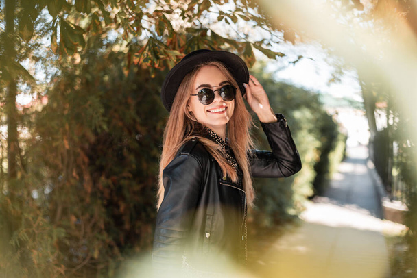 Счастливый осенний портрет красивой молодой женщины с улыбкой в модной черной одежде в шляпе выходит на улицу в солнечный день - Фото, изображение