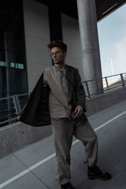Stylowy, przystojny młody mężczyzna w modnych ubraniach z kurtką i koszulą spaceruje po miejskim tle. mężczyzna casual styl wygląd - Zdjęcie, obraz