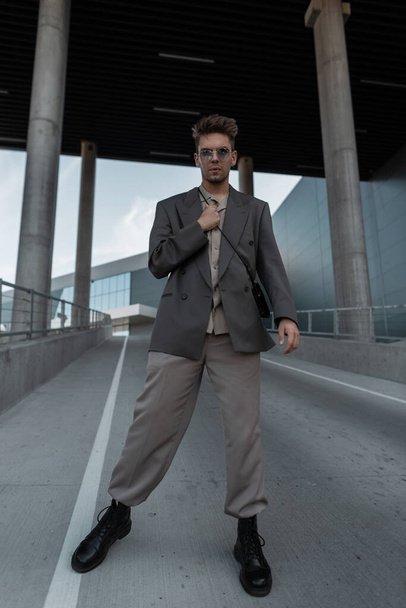 Fashion hipster man model in stylish blazer, shirt and boots walks in the city. Urban male style - Zdjęcie, obraz