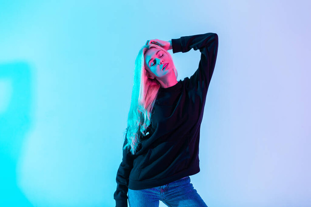 Muoti värikäs muotokuva kaunis nuori blondi nainen musta huppari sininen farkut poseeraa neon-vaaleanpunainen tausta studiossa - Valokuva, kuva