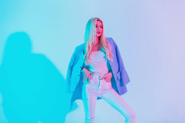 Modaya uygun güzel bir iş kızı, beyaz şık bir giysi içinde, mavi ceketli, renkli, neon renkli ışıklarıyla. - Fotoğraf, Görsel