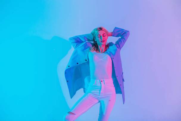 Stüdyoda parlak pembe ışıklı mavi ceketli, bluzlu ve beyaz kotlu zarif iş elbiseli genç ve seksi bir kadının çok renkli yaratıcı portresi. - Fotoğraf, Görsel