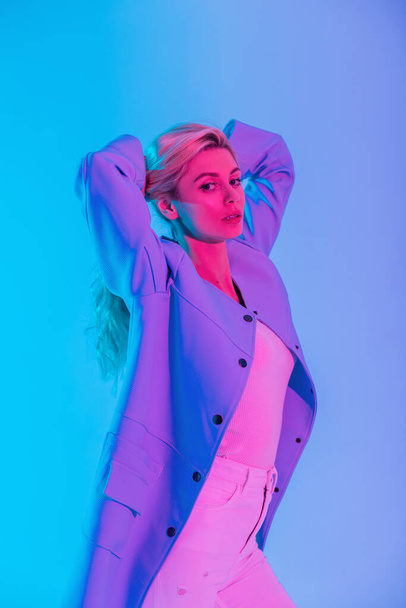 Modelo de chica de belleza de moda con elegante abrigo azul y blusa blanca con jeans en interiores con luz rosa de neón colorida - Foto, imagen