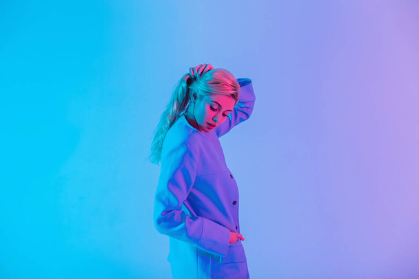 Female colored portrait of pretty stylish woman with fashionable clothes on multicolored neon and pink light indoors - Фото, изображение