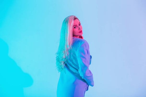 Fashion young business model girl with blue coat look to the camera in pastel colors neon pink lights in studio - Fotó, kép