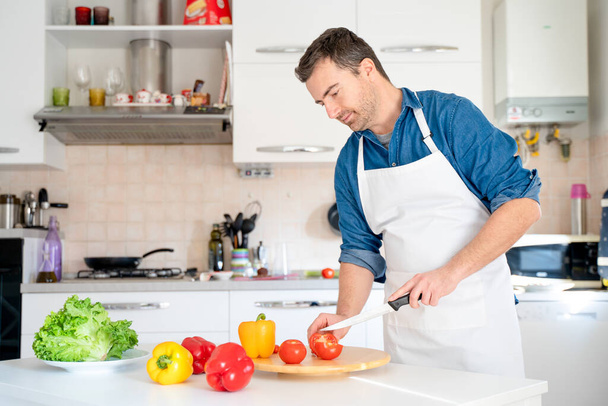 Retrato de un hombre cocinando en casa cortando verduras - Foto, Imagen