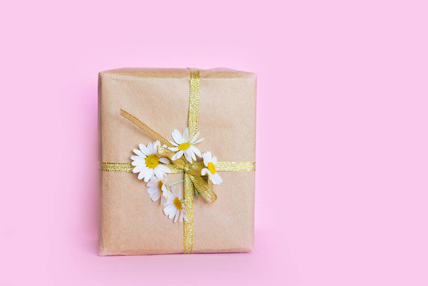 Gift in a box tied with a golden ribbon and a bouquet of daisies on a pink pastel background. Gift for March 8 or Mother's Day. - Foto, imagen