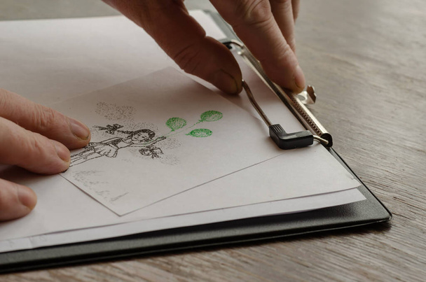 男の手は、タブレットに手描きの図面で紙のシートを押す。点線のペンの描画技術。紙の上に緑の風船で少女を描く。現代美術。選択的焦点. - 写真・画像