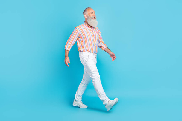 Full length profile side photo of aged man happy positive smile go walk look empty space isolated over blue color background - Foto, Imagen