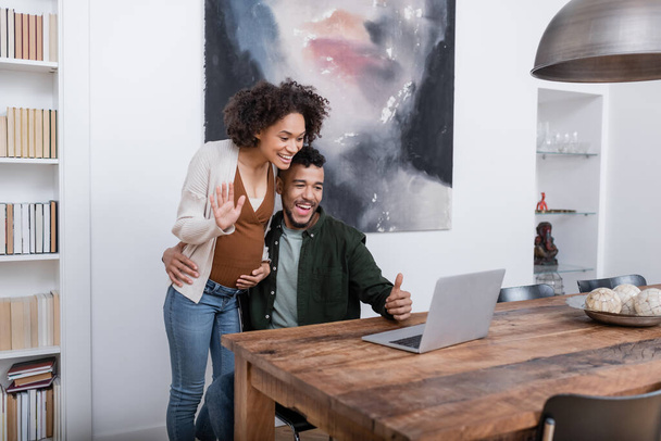 happy pregnant african american woman waving hand at laptop near husband showing thumb up - Photo, Image