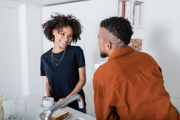 cheerful african american woman looking at blurred boyfriend in kitchen  - Foto, imagen
