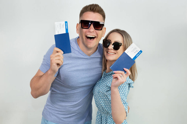 Cheerful young tourists in sunglasses, a guy and a girl isolated on a white background with passports and tickets in their hands - Φωτογραφία, εικόνα