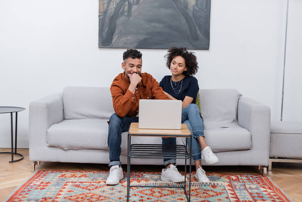 happy young african american couple smiling while watching movie on laptop in modern apartment  - Zdjęcie, obraz