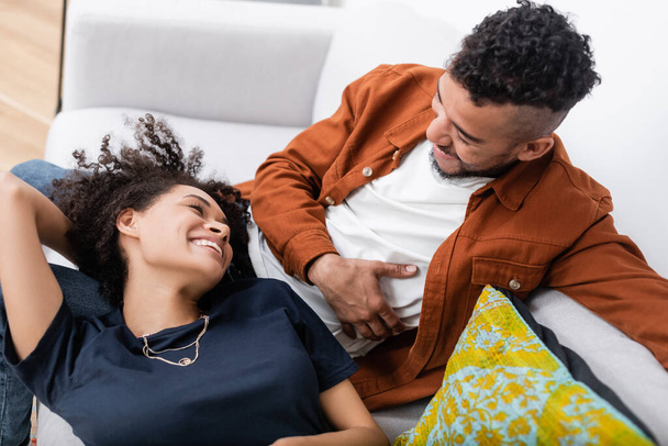 high angle view of cheerful african american couple looking at each other while resting on couch - Foto, Imagen