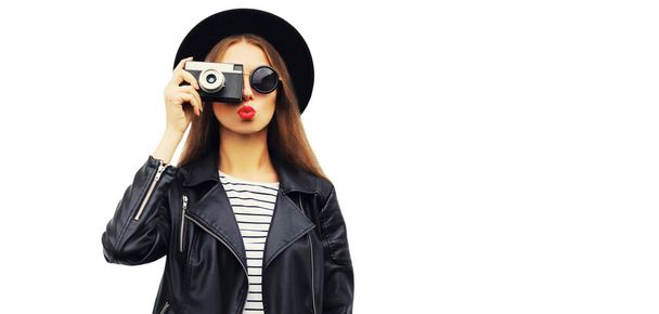 Stylish portrait of beautiful young woman photographer with vintage film camera wearing black round hat, leather jacket isolated on white background - Foto, imagen
