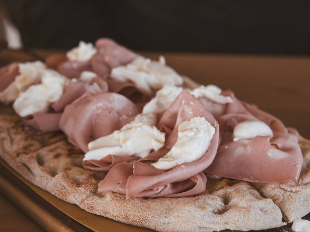 Close up wooden cutting board with typical Pinsa Romana on top topped with mozzarella and mortadella - Foto, afbeelding