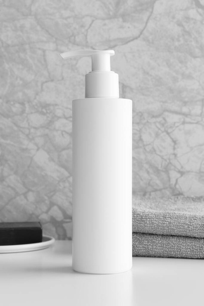 Weiße Shampoo-Spender Flasche Attrappe mit einer Seife und einem Handtuch auf dem weißen Tisch. - Foto, Bild