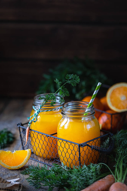 Healthy food. Carrots and carrot juice with orange in a glass jar in a metal basket on a dark wooden background. Copy space - Zdjęcie, obraz